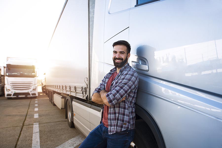 Trucking Insurance - Trucker Leans Against a White Truck, Arms Crossed, Smiling